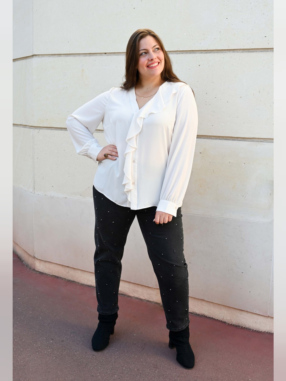 Chemise fluide écrue à jabot portée avec un jean noir, de face, en pied devant un mur clair