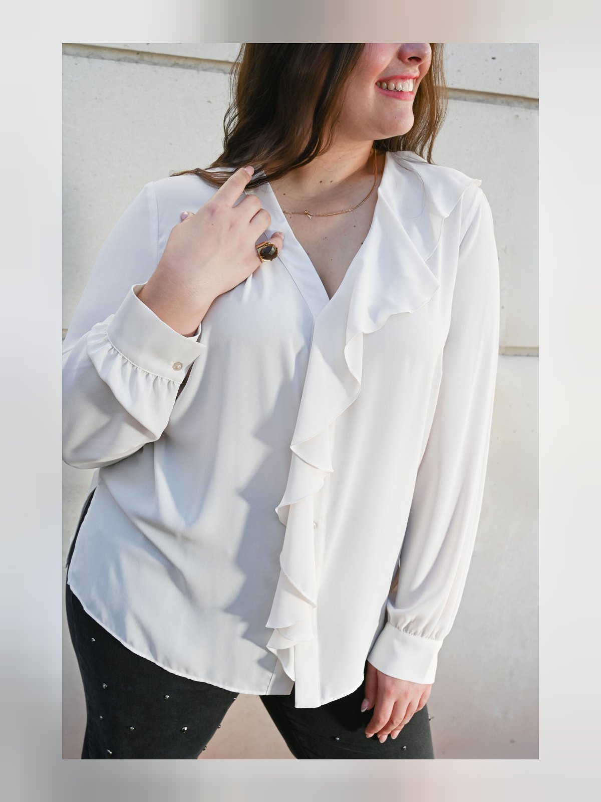 Gros plan sur le jabot de la chemise fluide écrue, encolure en V à froufrou et poignets boutonnés
