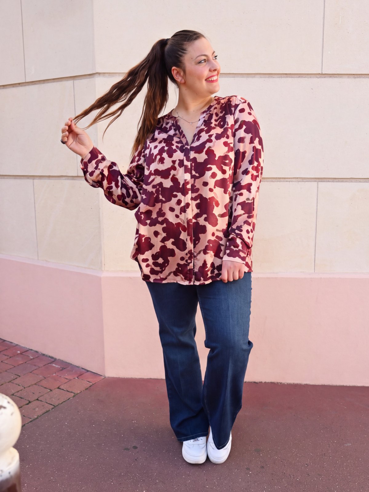 Femme portant une chemise fluide imprimée bordeaux sur fond bois de rose avec un jean bleu