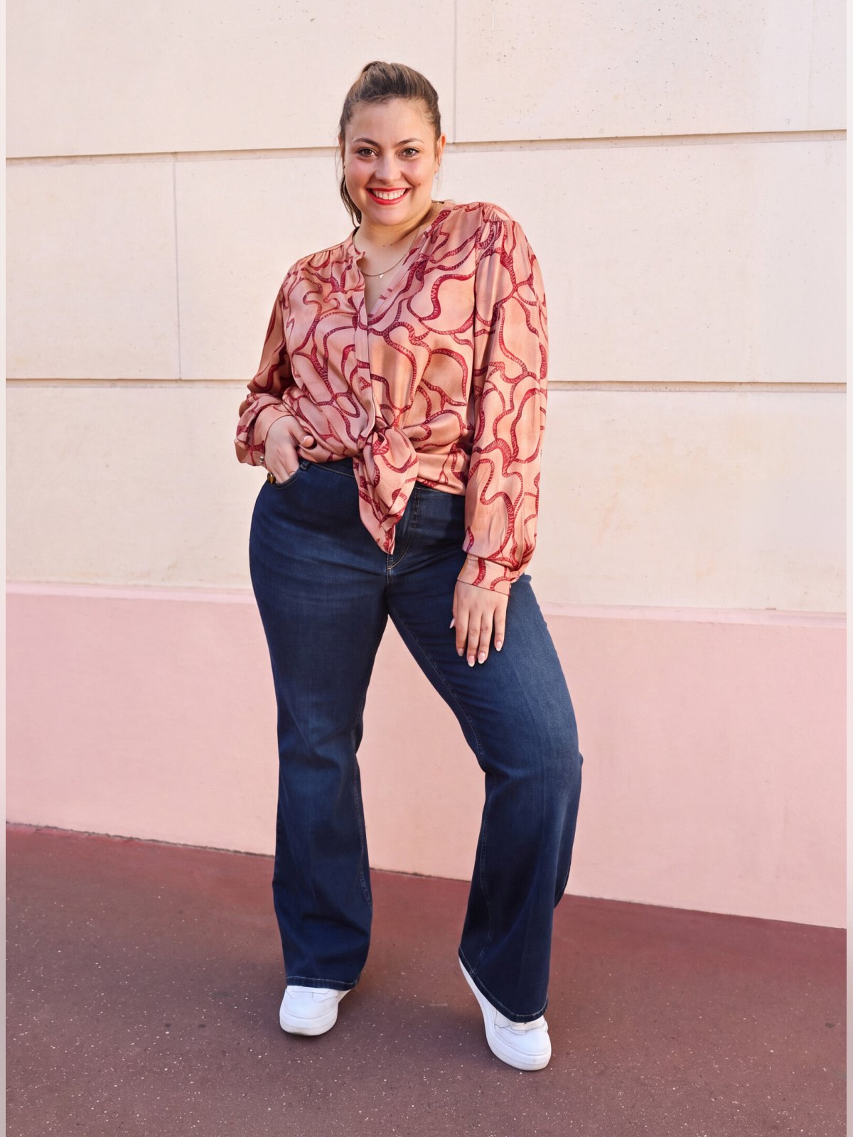 Chemise fluide imprimée sur fond bois de rose portée nouée à la taille avec un jean flare brut