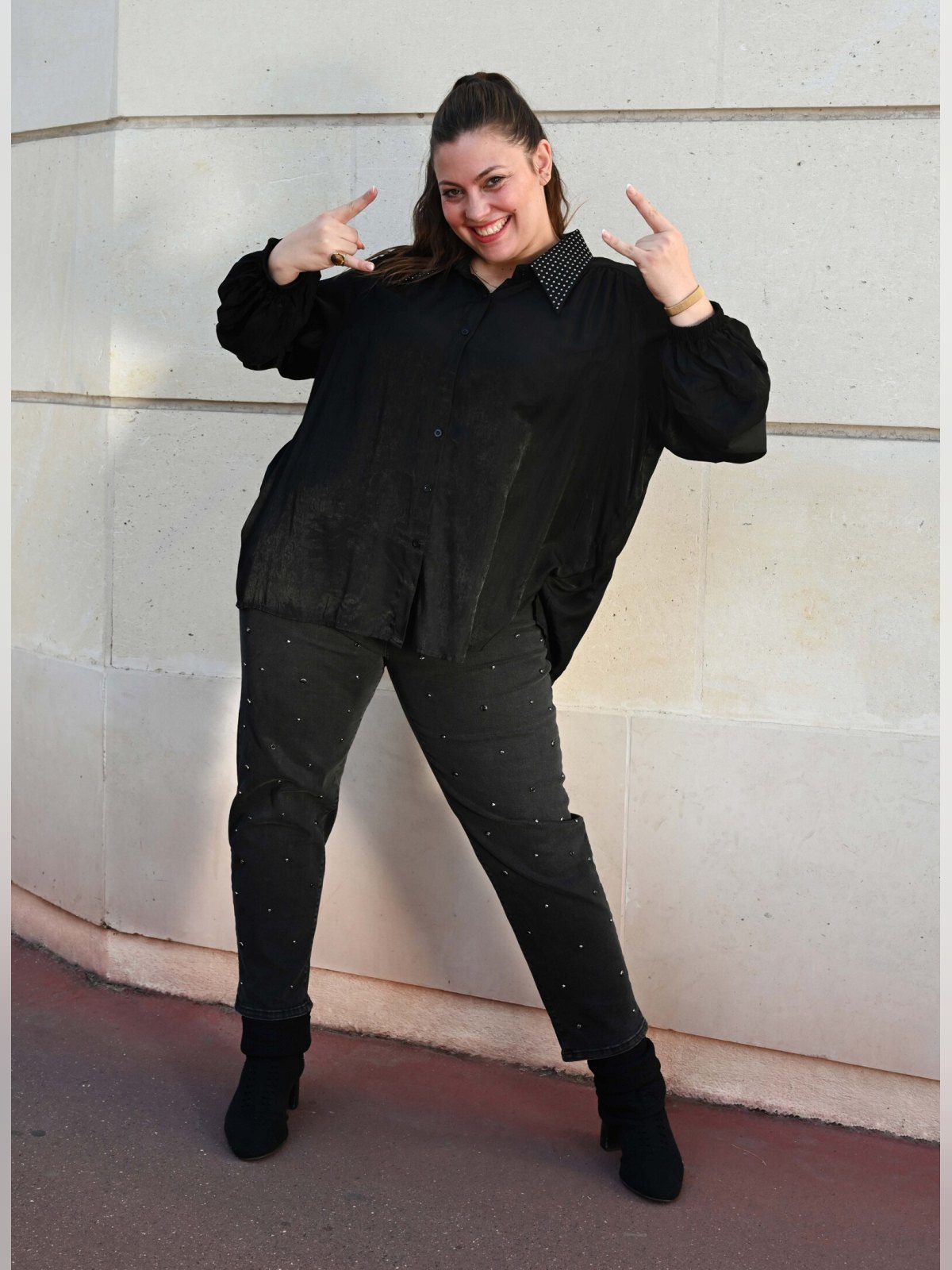 Chemise noire ample à col clouté portée ouverte en bas, de face, avec jean noir clouté pour un look rock