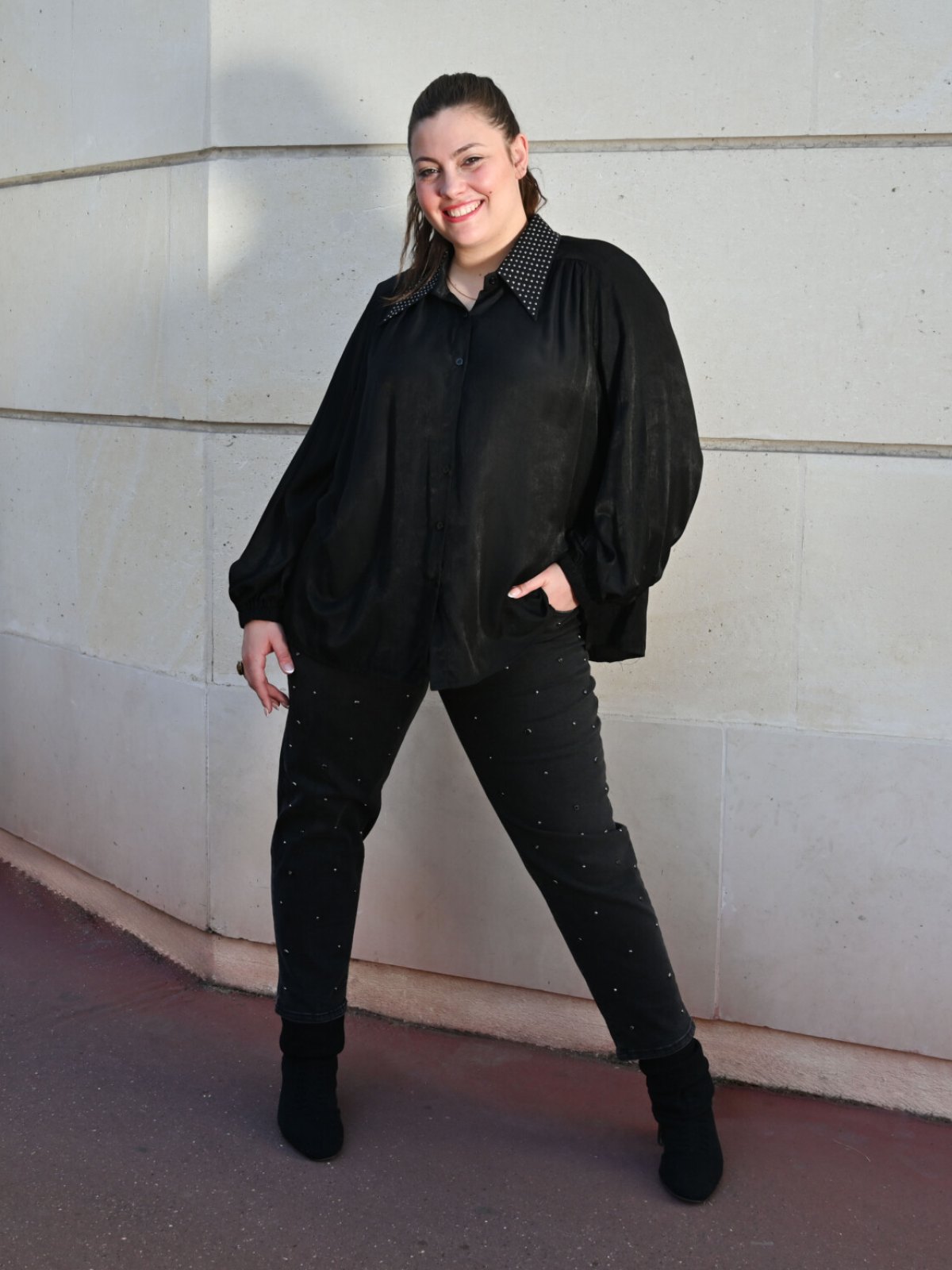Chemise noire fluide à col clouté et manches bouffantes portée avec un jean noir à clous et des bottines