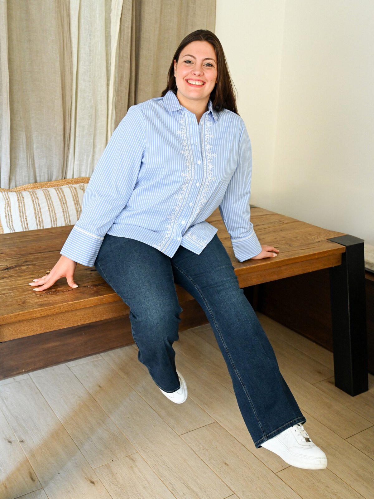 Chemise rayée bleu ciel à broderies blanches et manches longues, portée assise avec un jean