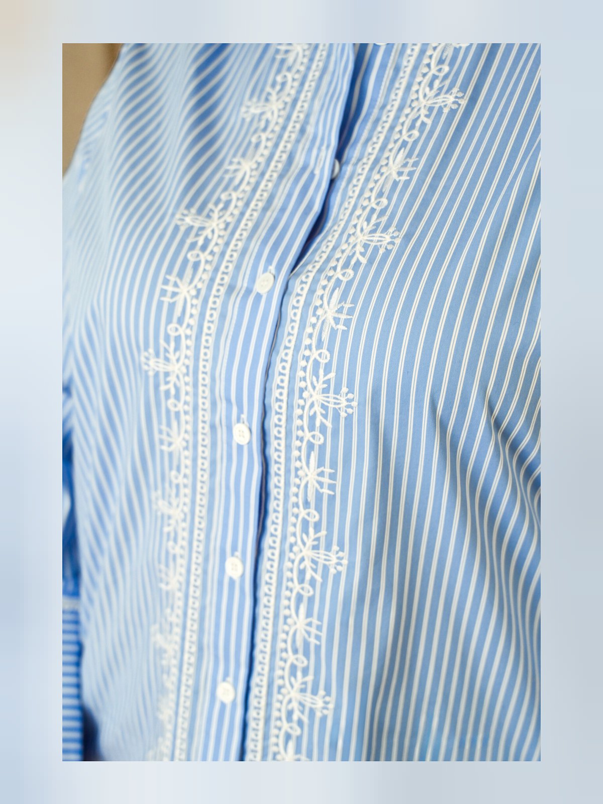 Gros plan sur les broderies blanches et les fines rayures bleu ciel d'une chemise boutonnée