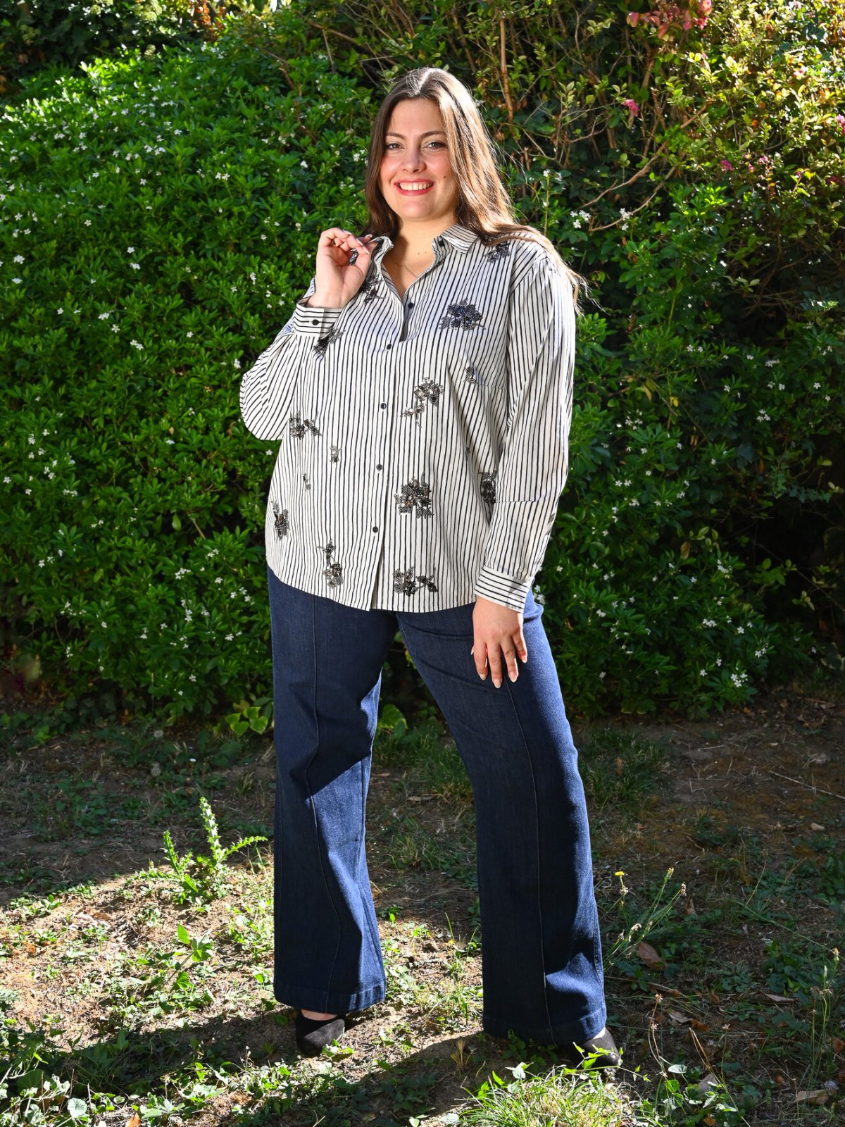 Chemise rayée noir et blanc à fleurs brodées portée avec un jean flare brut, vue de face en pied