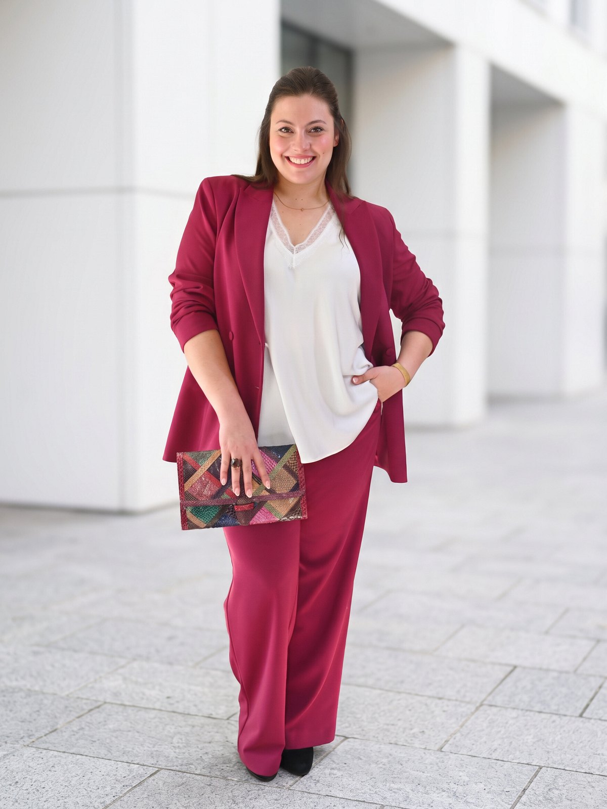 Débardeur blanc à encolure en dentelle porté sous un tailleur framboise avec une pochette colorée