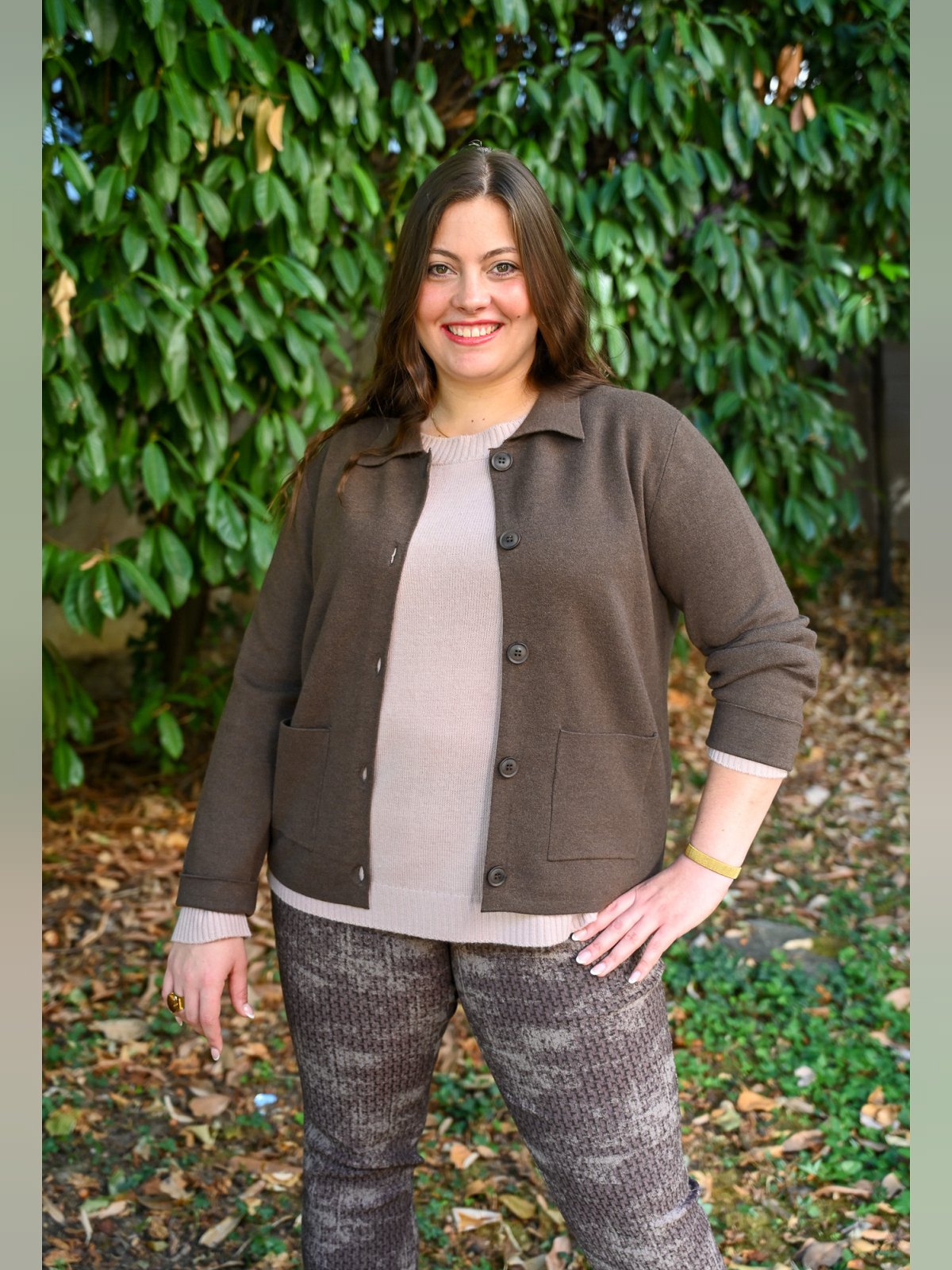 Femme souriante portant un gilet marron à col chemise et poches plaquées sur un pull beige