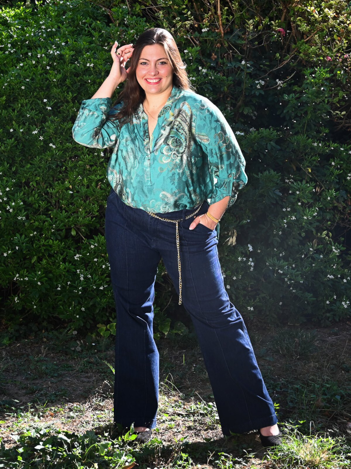 Jean large taille haute bleu brut avec ceinture chaîne dorée porté avec une blouse verte dans un jardin