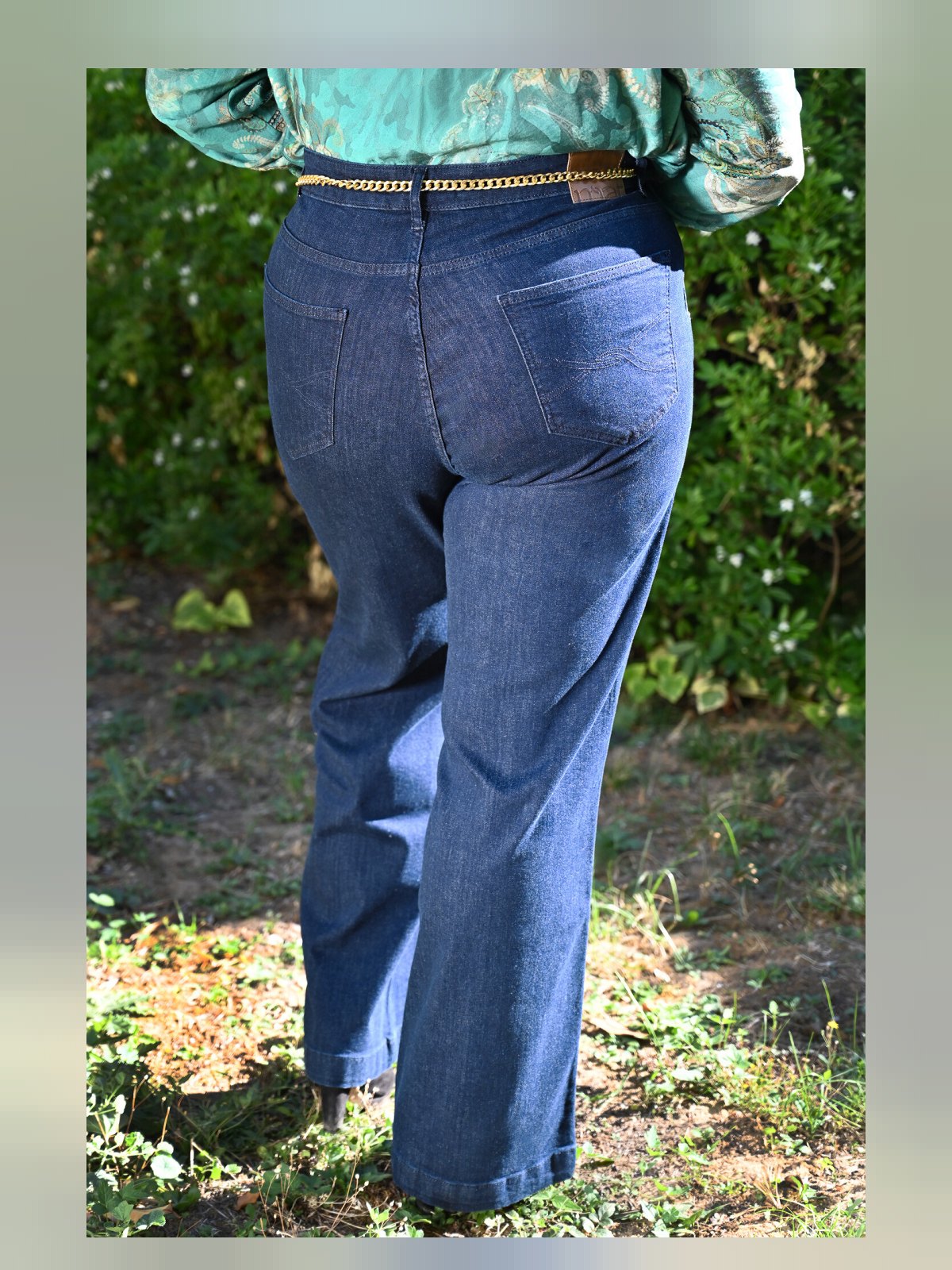 Dos du jean large bleu brut avec poches plaquées surpiquées, étiquette en cuir et chaîne dorée