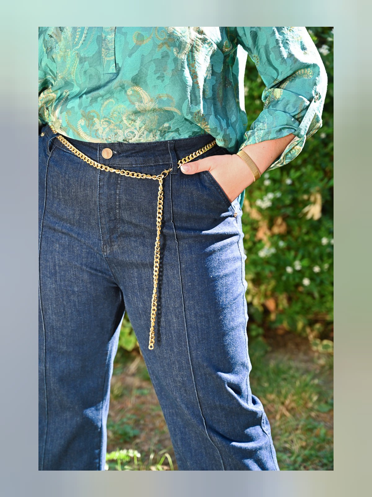 Gros plan sur la ceinture chaîne dorée, le bouton et la poche avant du jean taille haute bleu brut