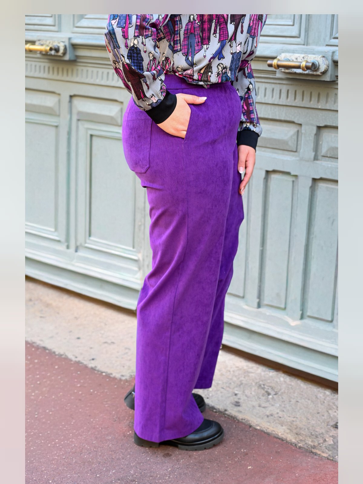 Pantalon en velours côtelé violet vu de profil, coupe large et jambe droite, main dans la poche