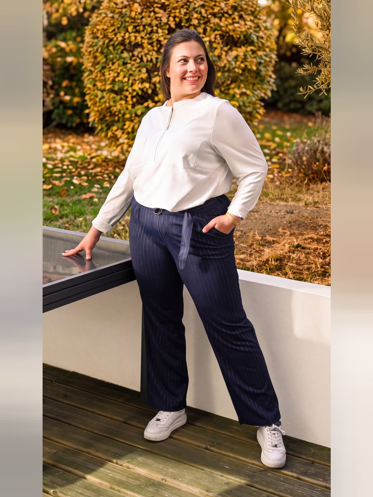 Pantalon marine à fines rayures blanches porté avec une blouse blanche et des baskets, vue de face en pied