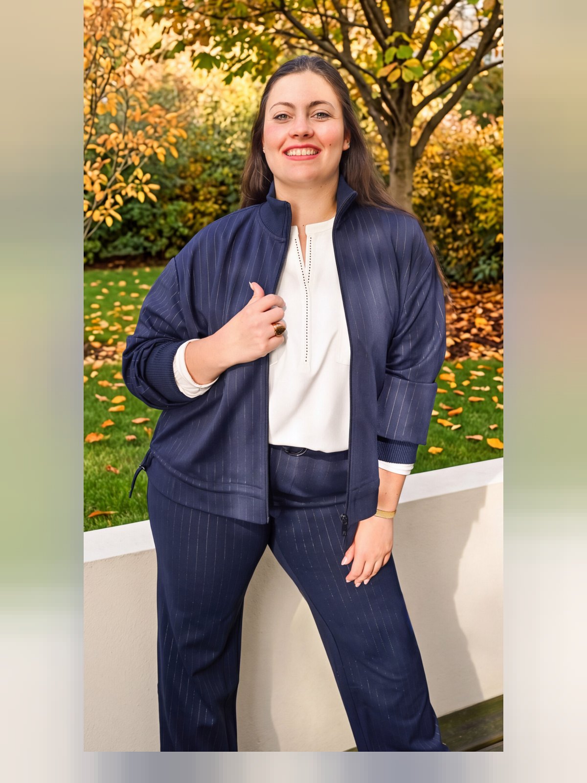 Pantalon marine à fines rayures blanches porté en total look avec sa veste zippée assortie et une blouse blanche