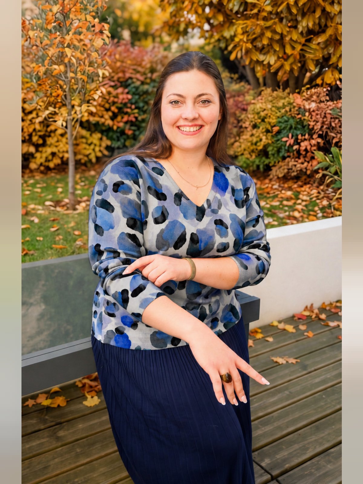 Femme souriante portant un pull col V à imprimé léopard bleu, gris et noir dans un jardin d'automne