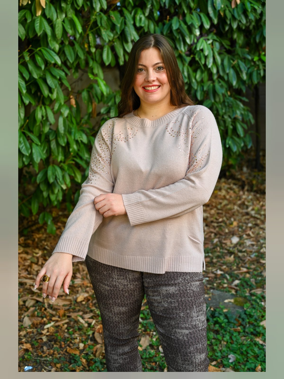 Pull beige rosé à col rond orné de strass dorés porté avec un pantalon gris chiné