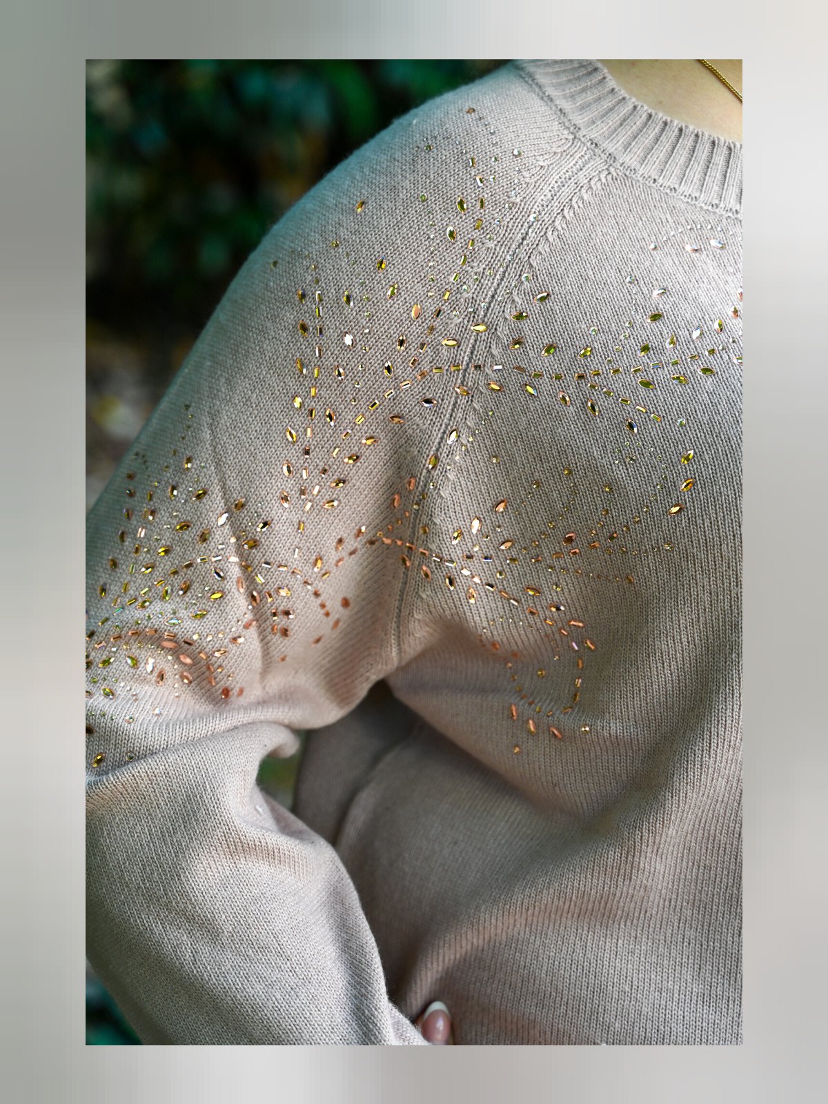 Gros plan sur les strass dorés et la maille fine de l'épaule raglan du pull beige rosé