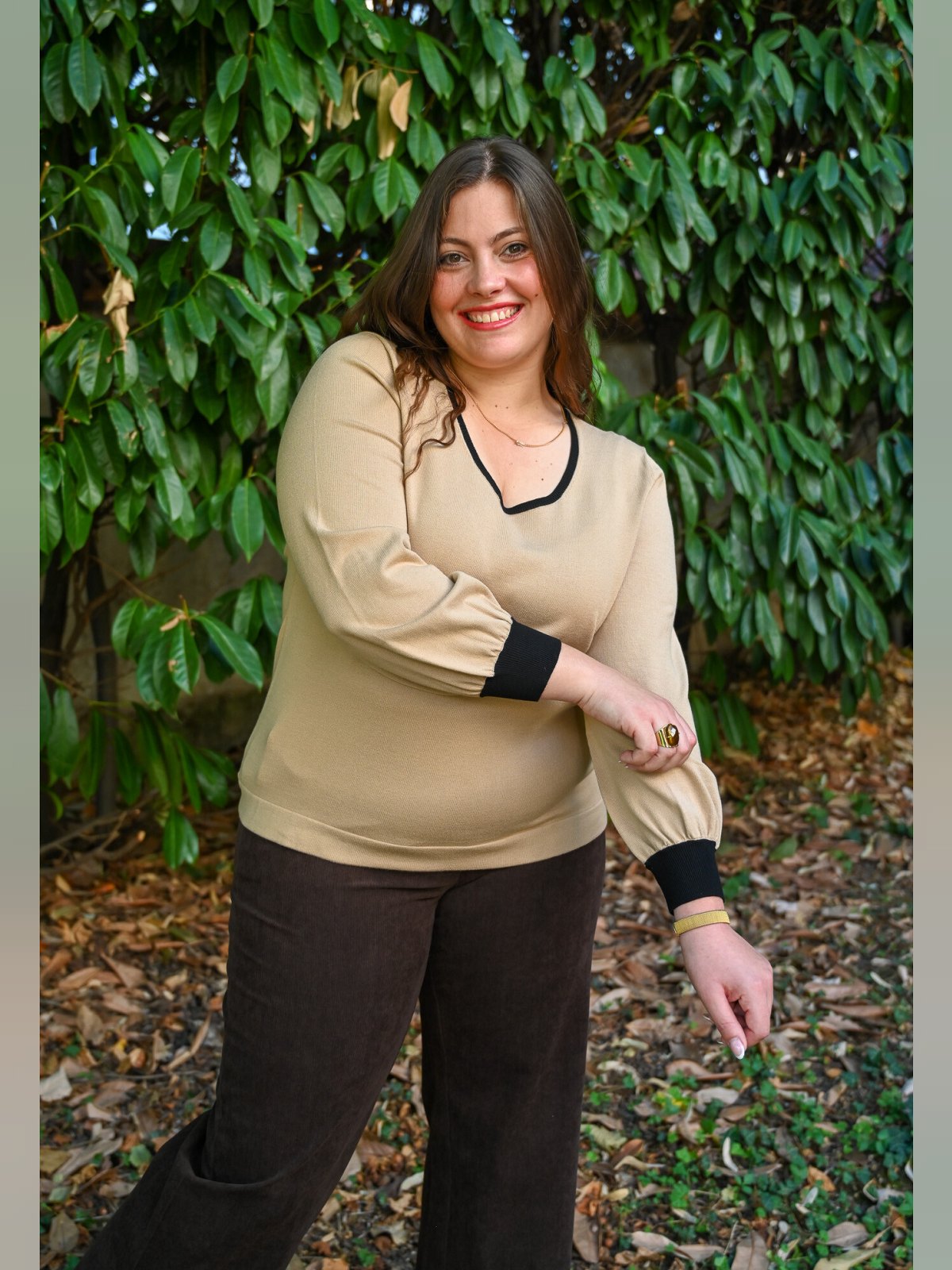 Pull en maille camel à encolure V liserée de noir et poignets noirs, porté avec un pantalon marron