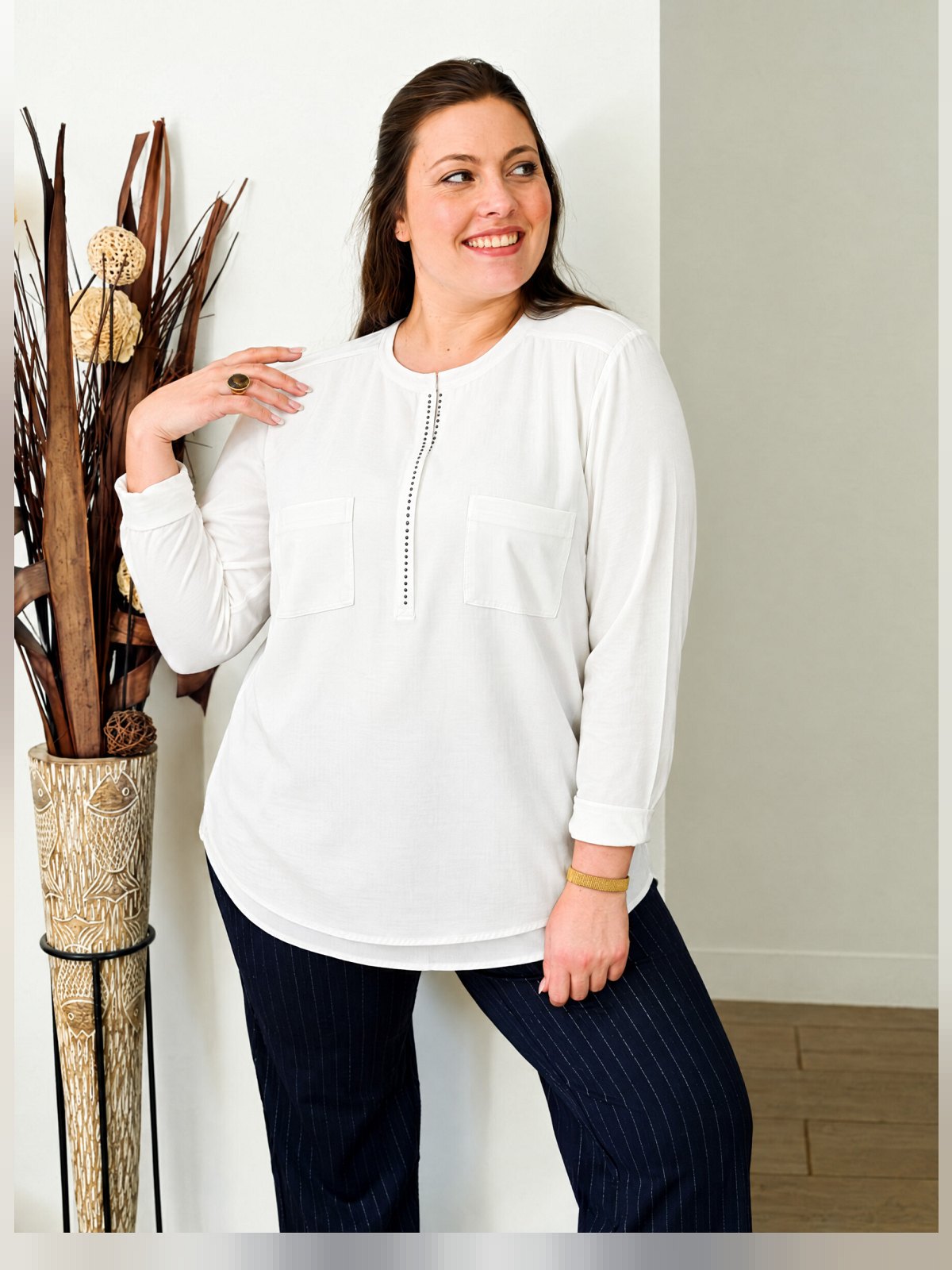 Tunique blanche bi-matière à manches longues et strass noirs, portée de face avec un pantalon rayé