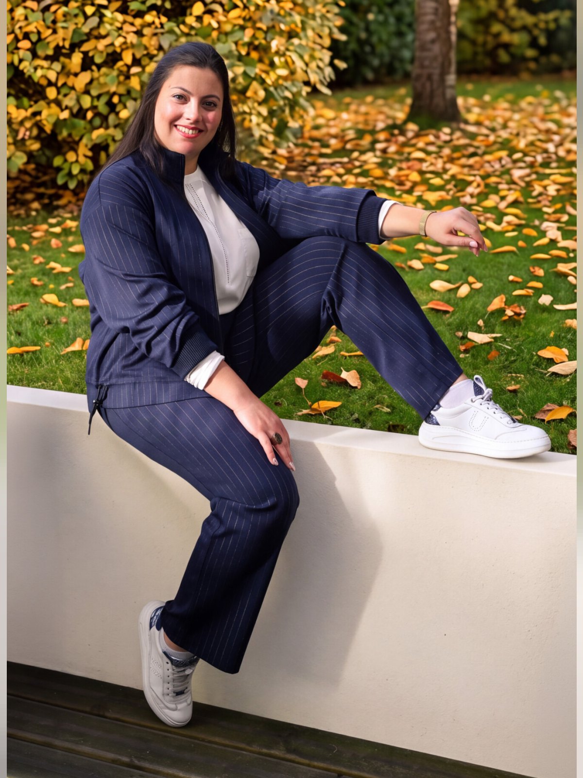 Veste marine à fines rayures et fermeture zip portée en total look avec le pantalon assorti, mannequin assise